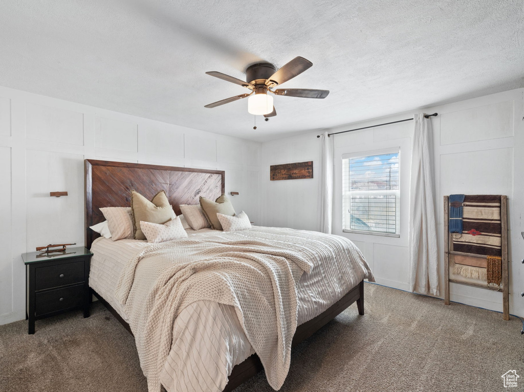 Carpeted bedroom featuring a decorative wall, a textured ceiling, and a ceiling fan