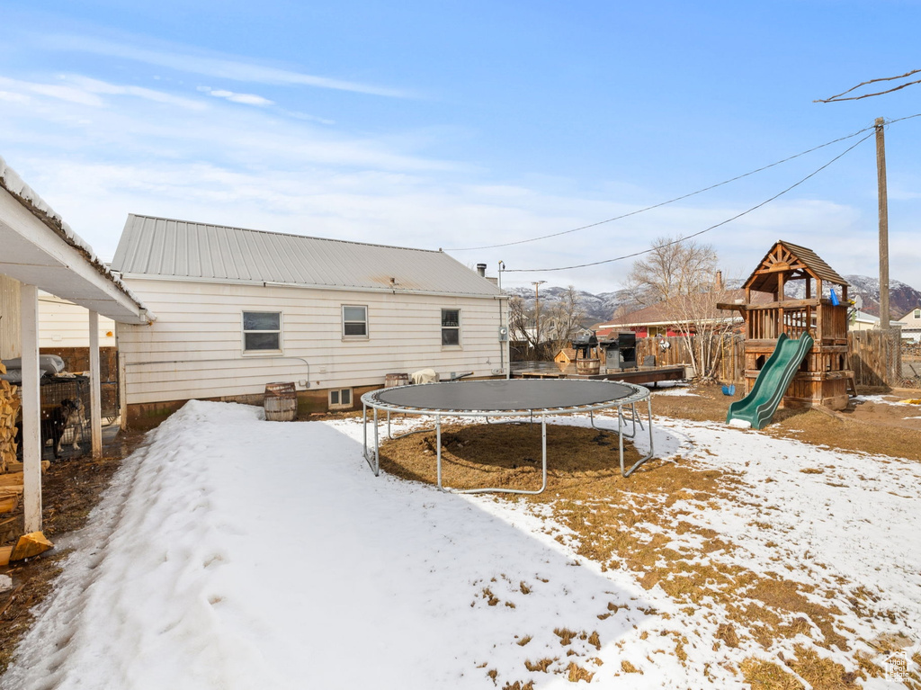Snow covered property featuring a playground, a trampoline, and metal roof