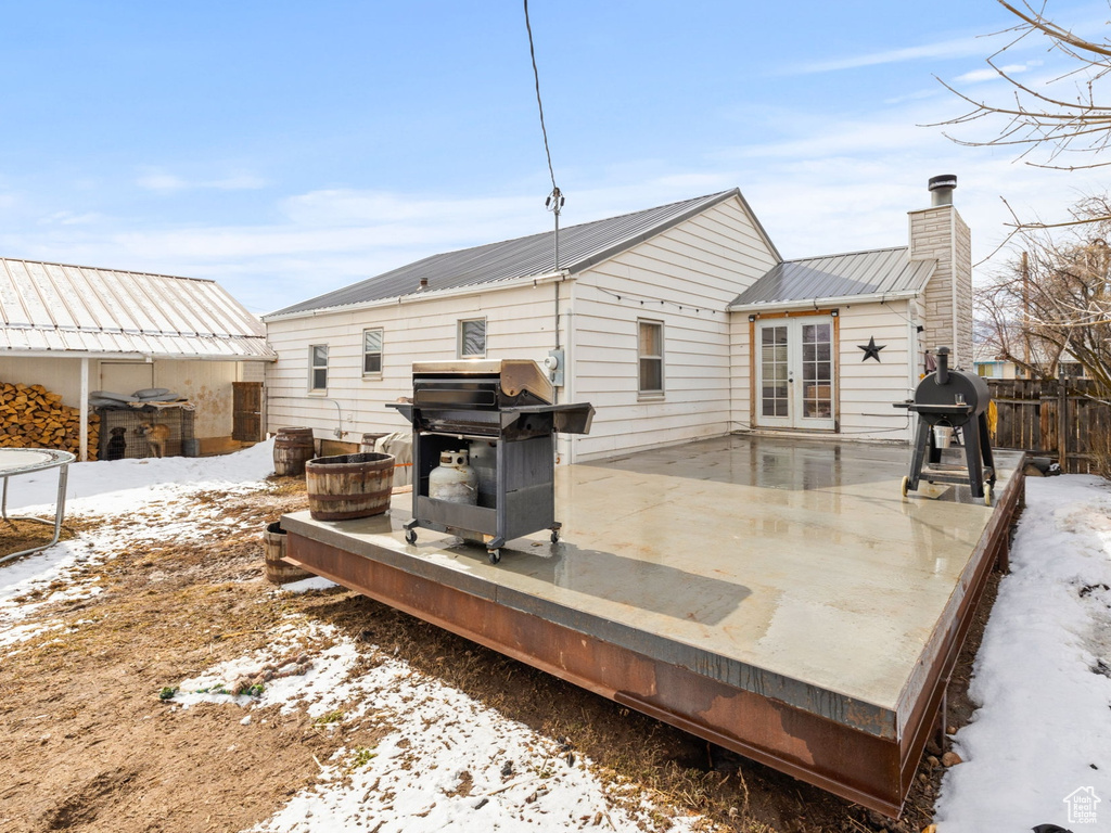 Snow covered property with french doors, metal roof, a chimney, and fence