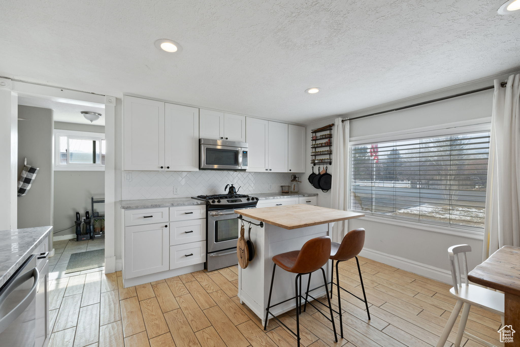 Kitchen with light wood-style flooring, stainless steel appliances, decorative backsplash, white cabinetry, and butcher block counters