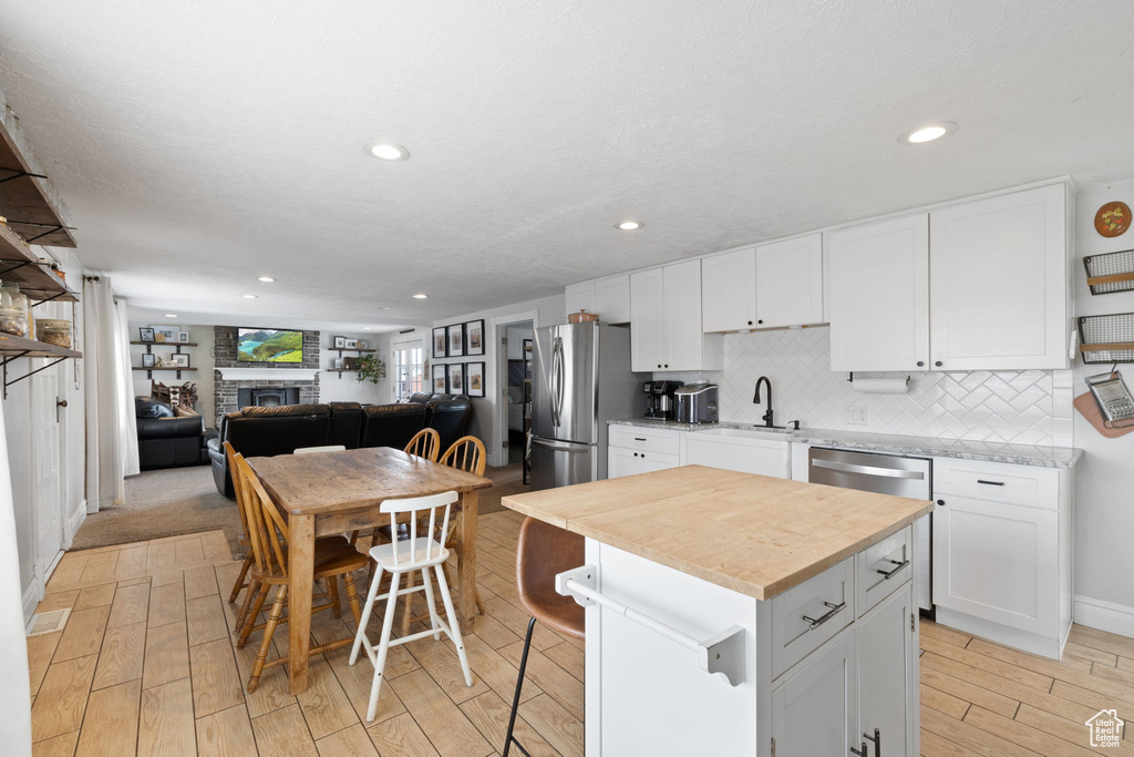 Kitchen featuring tasteful backsplash, light wood-style flooring, appliances with stainless steel finishes, a fireplace, and white cabinets