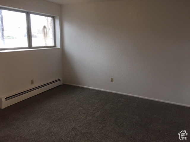 Spare room with dark colored carpet, a baseboard heating unit, and baseboards