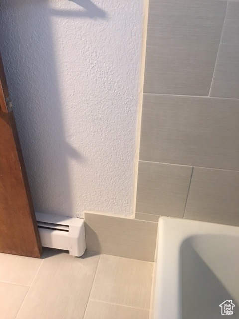 Details featuring a textured wall, a tub, and baseboard heating