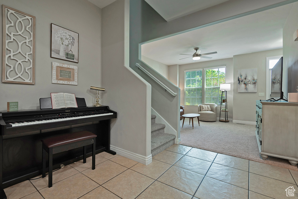 Foyer with a ceiling fan, light colored carpet, stairs, baseboards, and light tile patterned flooring