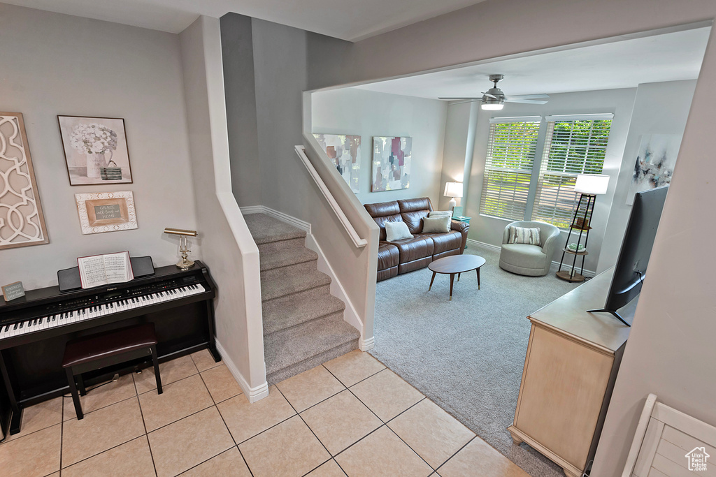 Living room with light carpet, a ceiling fan, baseboards, stairs, and light tile patterned floors