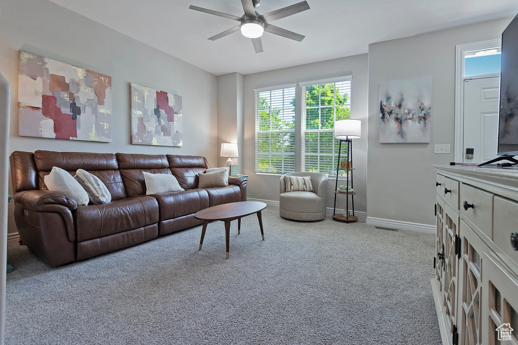 Carpeted living area with ceiling fan, baseboards, and plenty of natural light