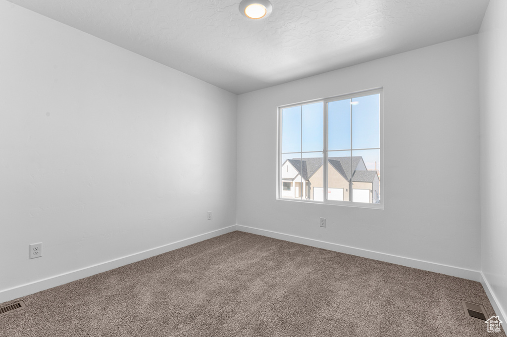 Spare room with carpet flooring, visible vents, a textured ceiling, and baseboards