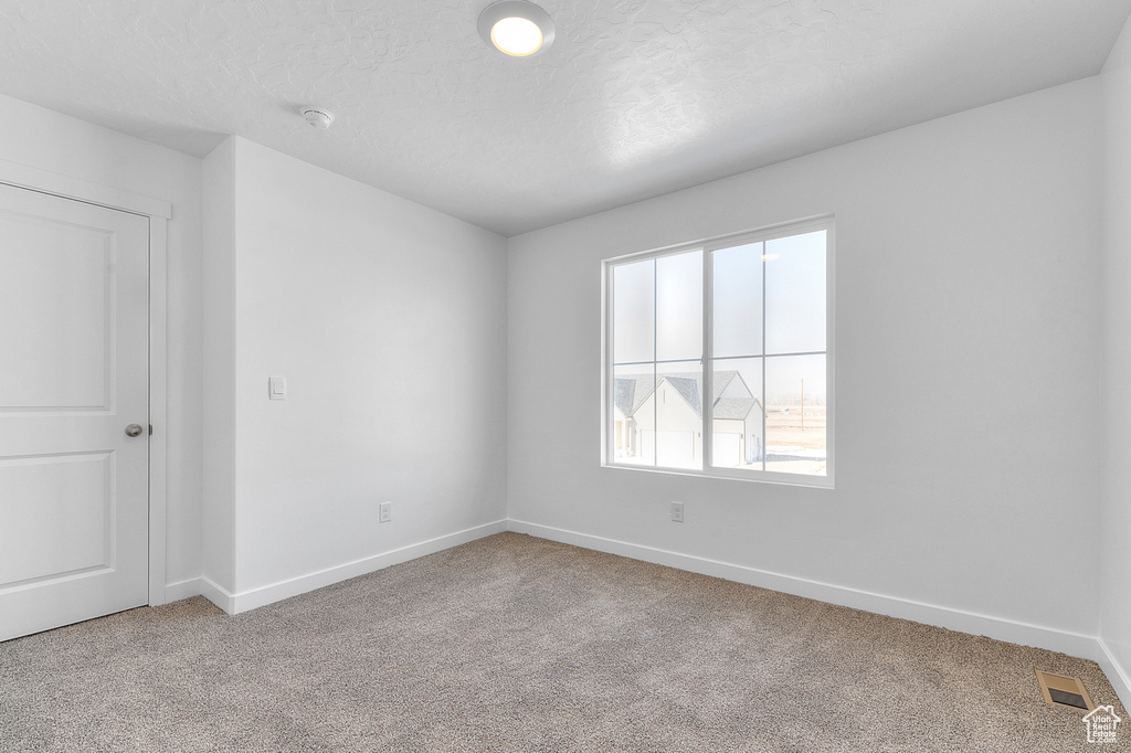 Unfurnished room featuring visible vents, light carpet, a textured ceiling, and baseboards