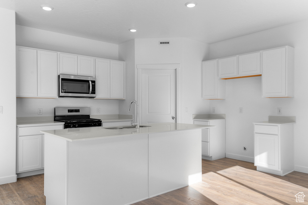 Kitchen featuring a center island with sink, a sink, white cabinets, appliances with stainless steel finishes, and light wood-type flooring