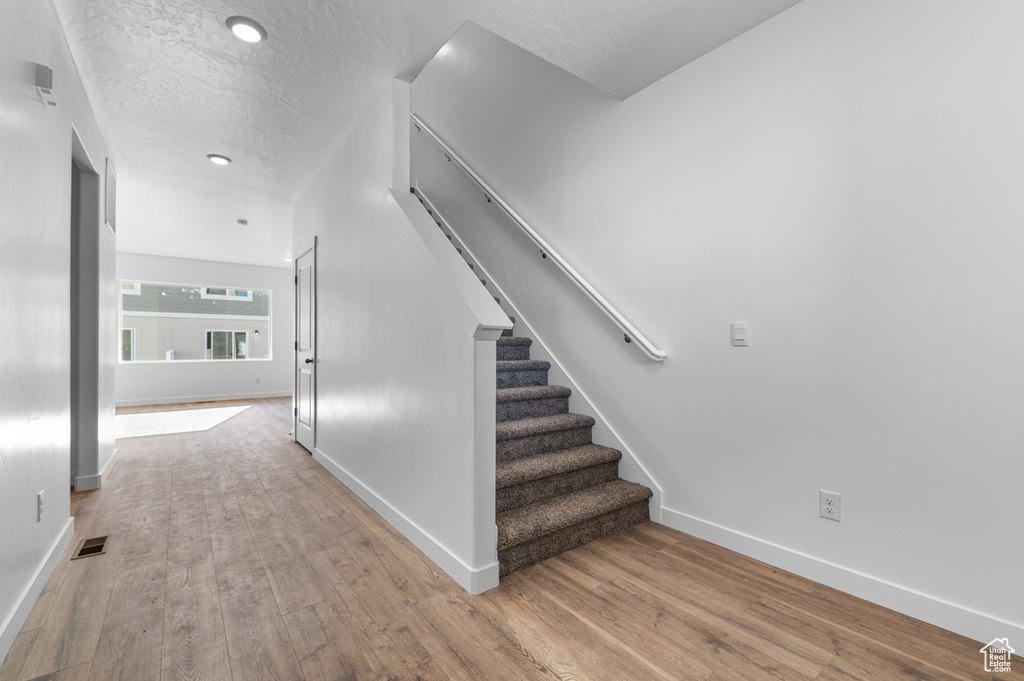 Staircase with visible vents, a textured ceiling, baseboards, and wood finished floors