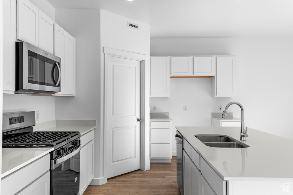 Kitchen with a sink, stainless steel appliances, wood finished floors, and white cabinetry