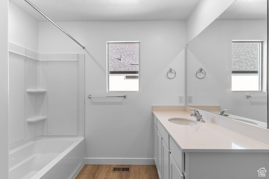 Bathroom featuring vanity, wood finished floors, visible vents, baseboards, and bathing tub / shower combination