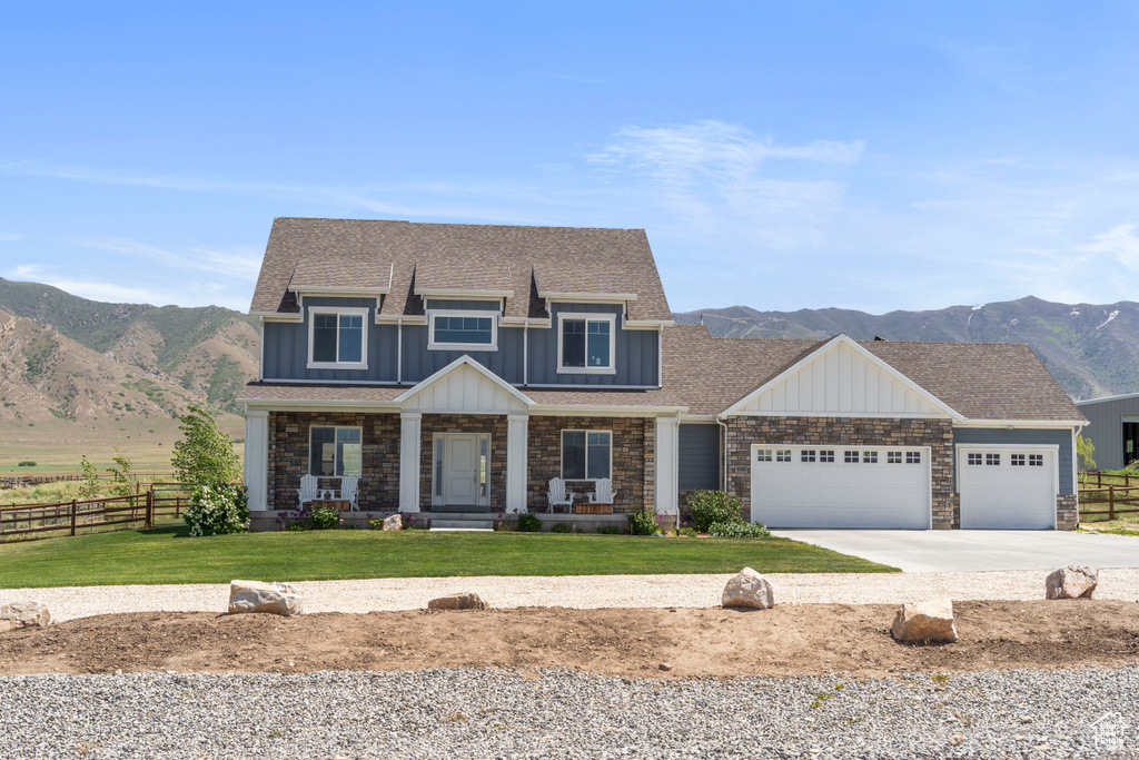 View of front facade featuring board and batten siding, a mountain view, driveway, covered porch, and an attached garage