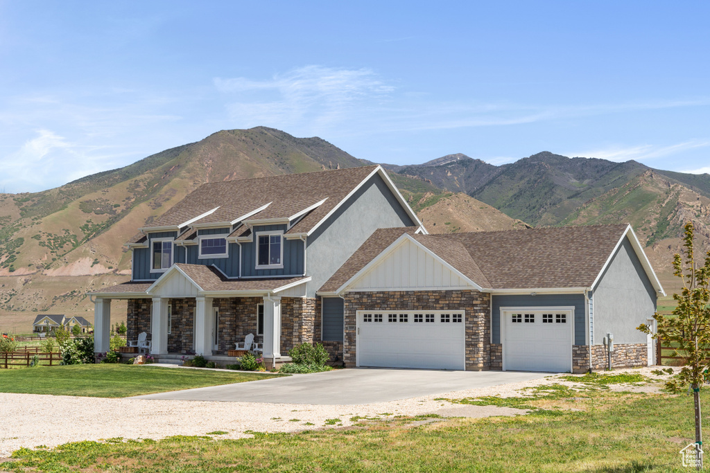 View of front of property with an attached garage, stone siding, covered porch, driveway, and a mountain view