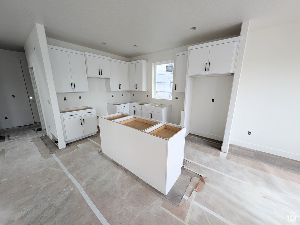 Kitchen featuring a kitchen island, white cabinets, washing machine and dryer, and baseboards