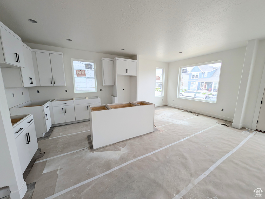Kitchen with plenty of natural light, a kitchen island, white cabinets, a textured ceiling, and concrete floors
