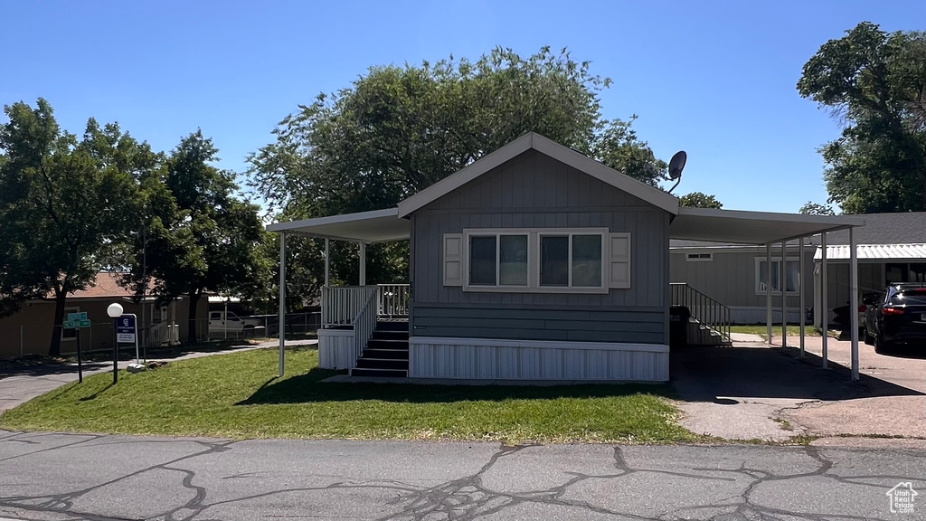 Manufactured / mobile home featuring stairs, a front lawn, and an attached carport