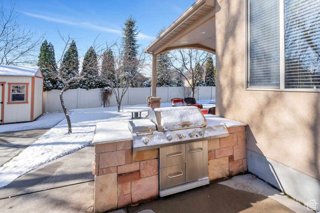 Snow covered patio with a storage shed, area for grilling, an outbuilding, and a fenced backyard
