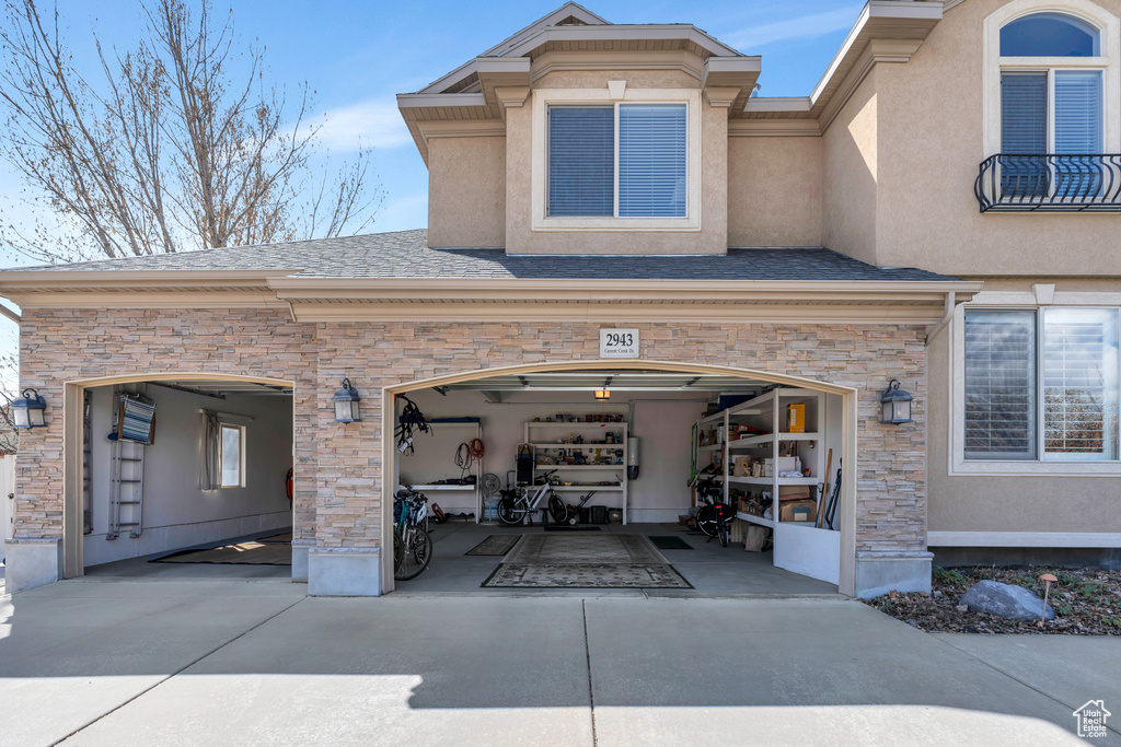 Exterior space with an attached garage, stucco siding, stone siding, and concrete driveway