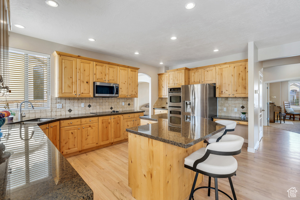 Kitchen featuring a center island, arched walkways, a sink, dark stone counters, and stainless steel appliances