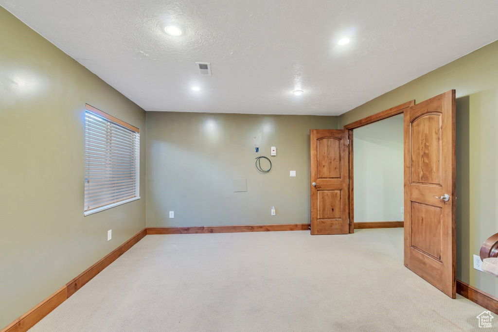 Empty room with a textured ceiling, light colored carpet, visible vents, recessed lighting, and baseboards