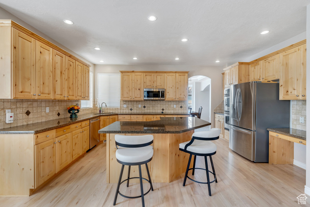 Kitchen featuring arched walkways, a sink, light wood-type flooring, appliances with stainless steel finishes, and light brown cabinetry
