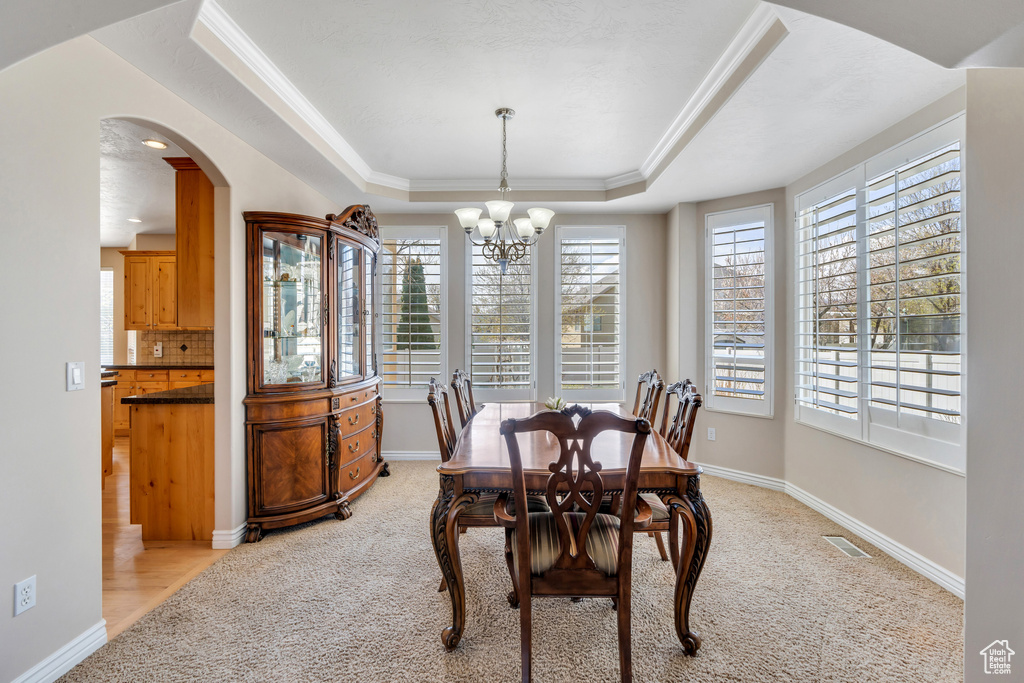 Dining space with visible vents, a raised ceiling, arched walkways, an inviting chandelier, and light carpet