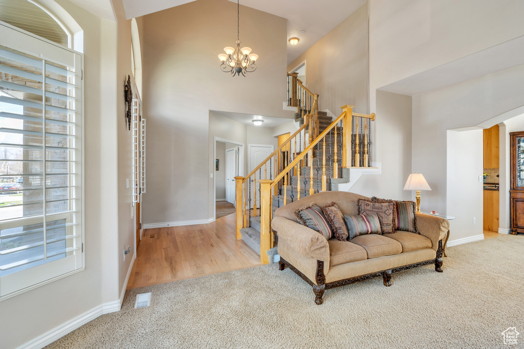 Living area with an inviting chandelier, carpet, visible vents, stairway, and a high ceiling
