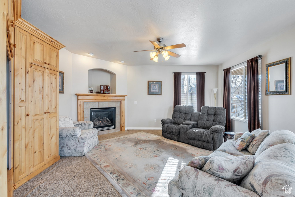 Living area featuring a tile fireplace, light colored carpet, ceiling fan, and baseboards