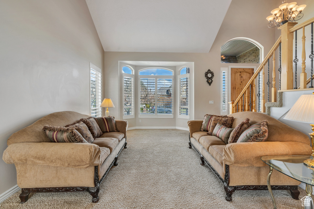 Carpeted living room with baseboards, high vaulted ceiling, a notable chandelier, and stairs