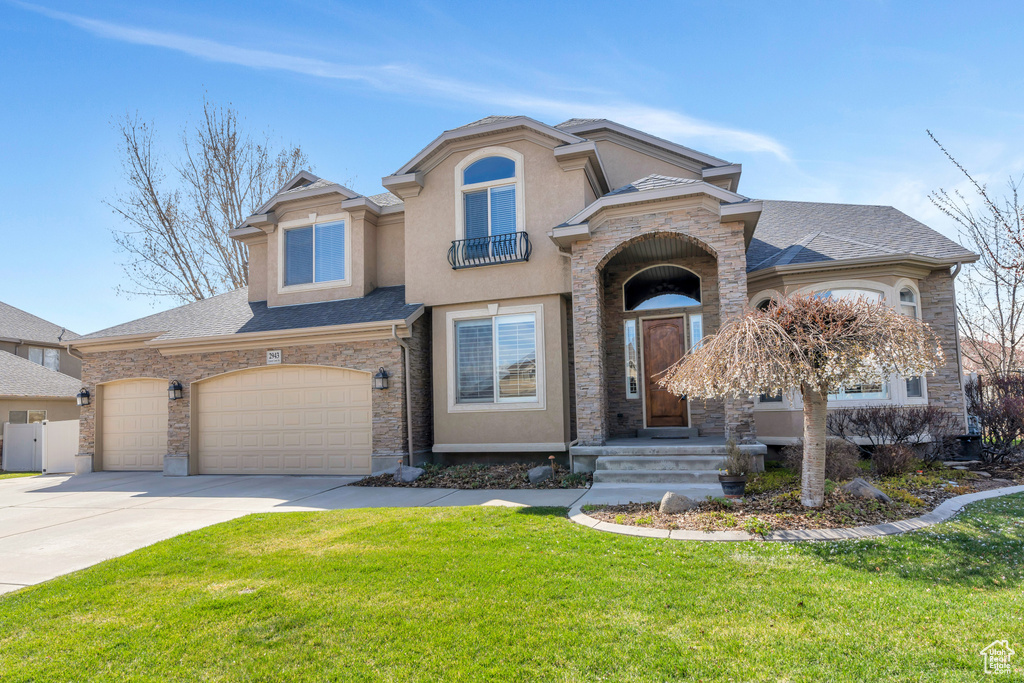 View of front of property featuring a balcony, stucco siding, driveway, a front yard, and a shingled roof