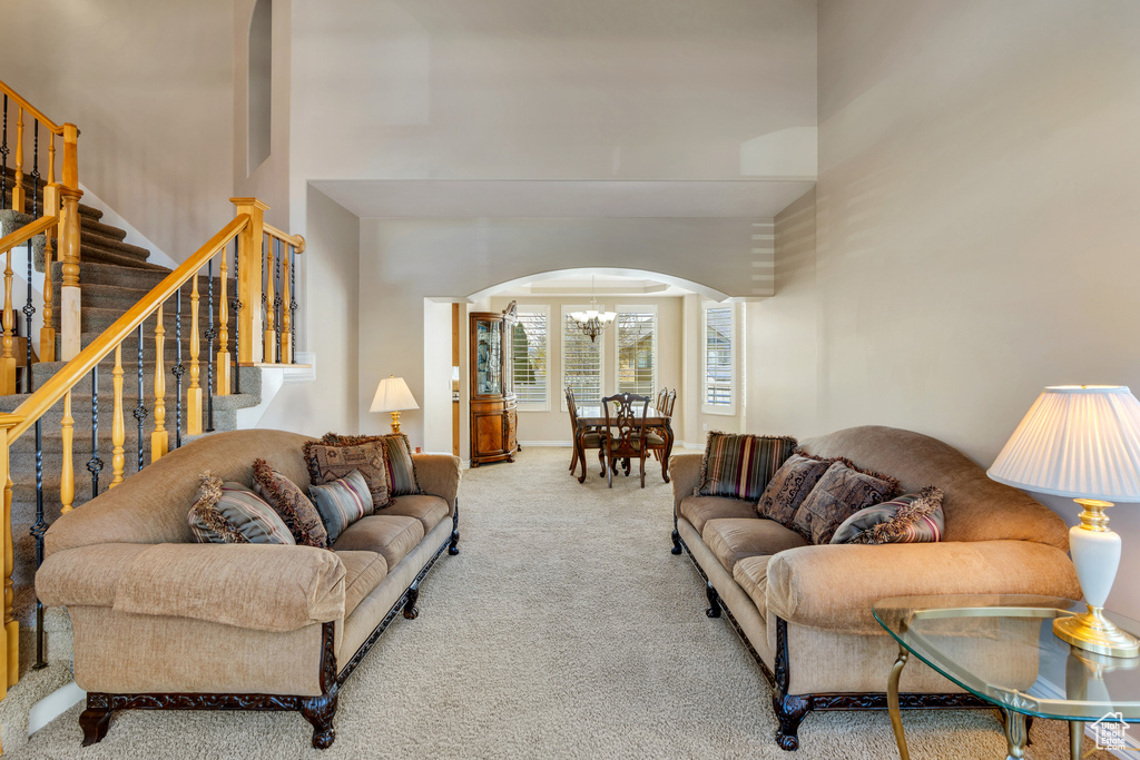 Living area with arched walkways, a notable chandelier, carpet, a towering ceiling, and stairs