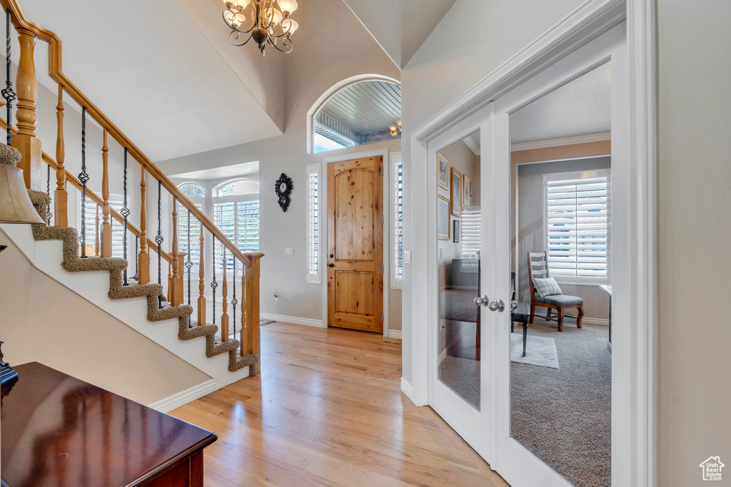 Foyer with french doors, light wood finished floors, a notable chandelier, and stairs