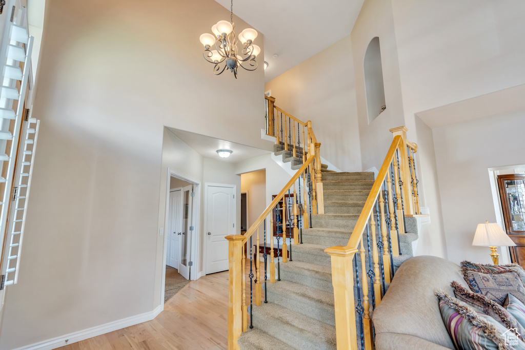 Stairs with a high ceiling, wood finished floors, baseboards, and a chandelier