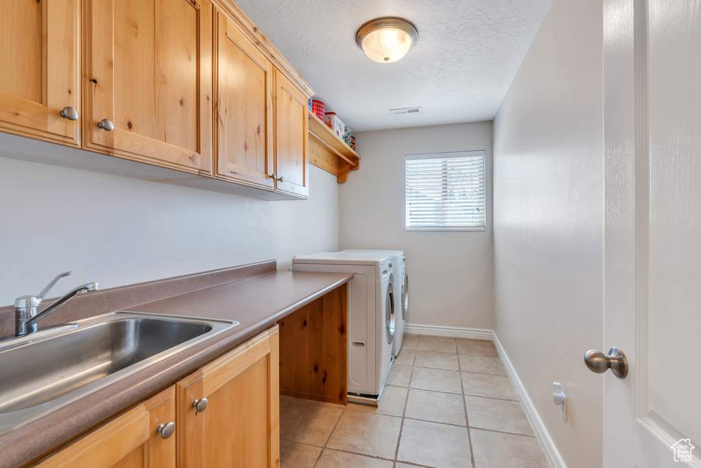 Washroom featuring light tile patterned floors, washing machine and dryer, a textured ceiling, cabinet space, and a sink