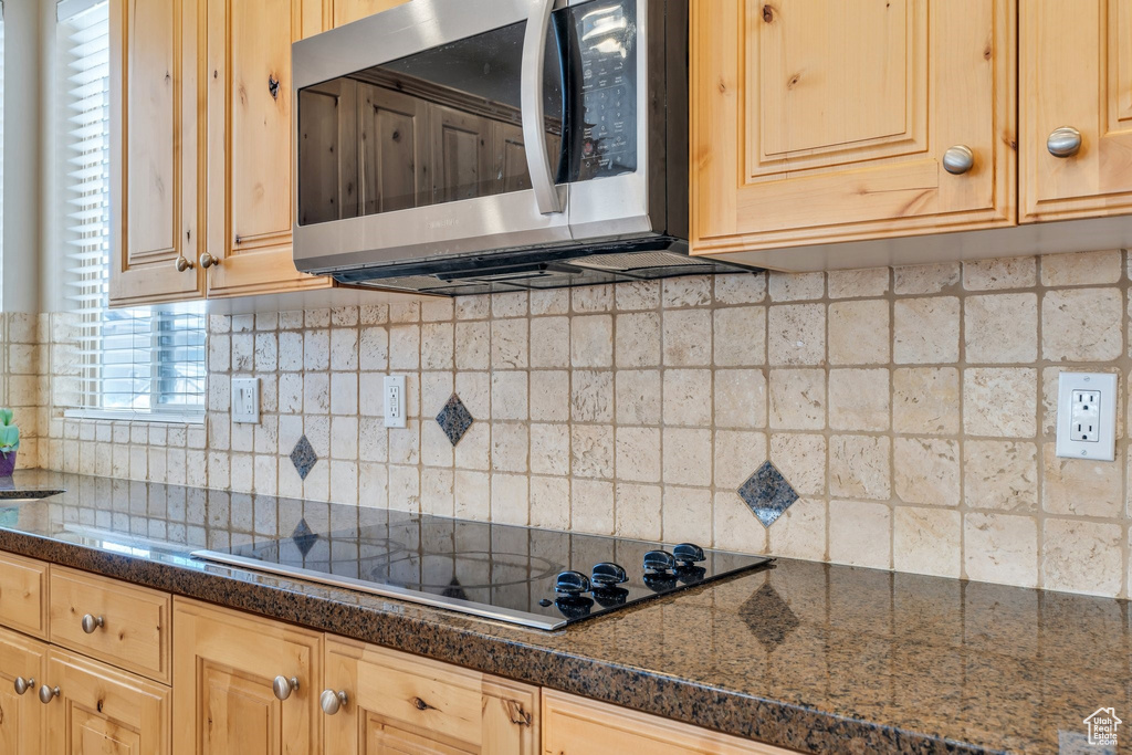 Kitchen with stainless steel microwave, light brown cabinets, black electric stovetop, backsplash, and dark countertops