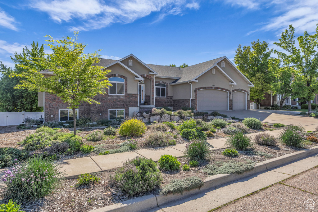 View of front of home with an attached garage, stucco siding, concrete driveway, fence, and brick siding