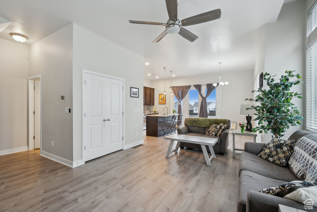 Living area featuring recessed lighting, ceiling fan with notable chandelier, baseboards, and light wood-style floors
