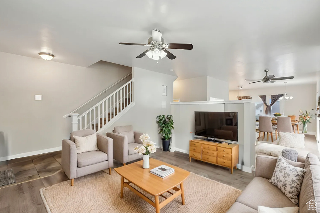 Living room featuring stairs, baseboards, wood finished floors, and a ceiling fan