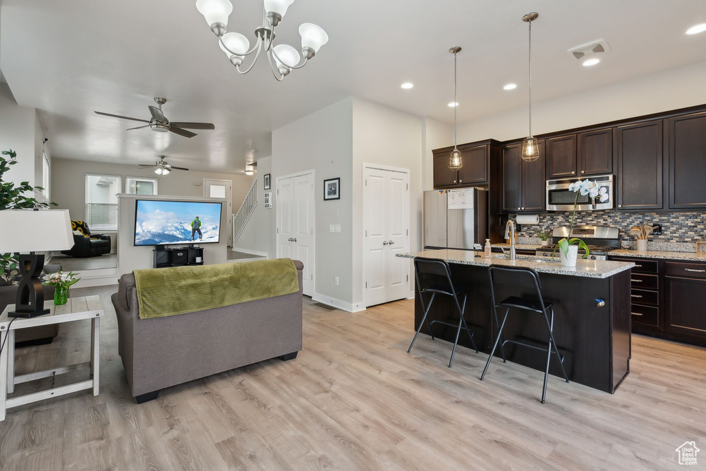 Kitchen featuring light wood-style flooring, ceiling fan with notable chandelier, tasteful backsplash, dark brown cabinetry, and appliances with stainless steel finishes