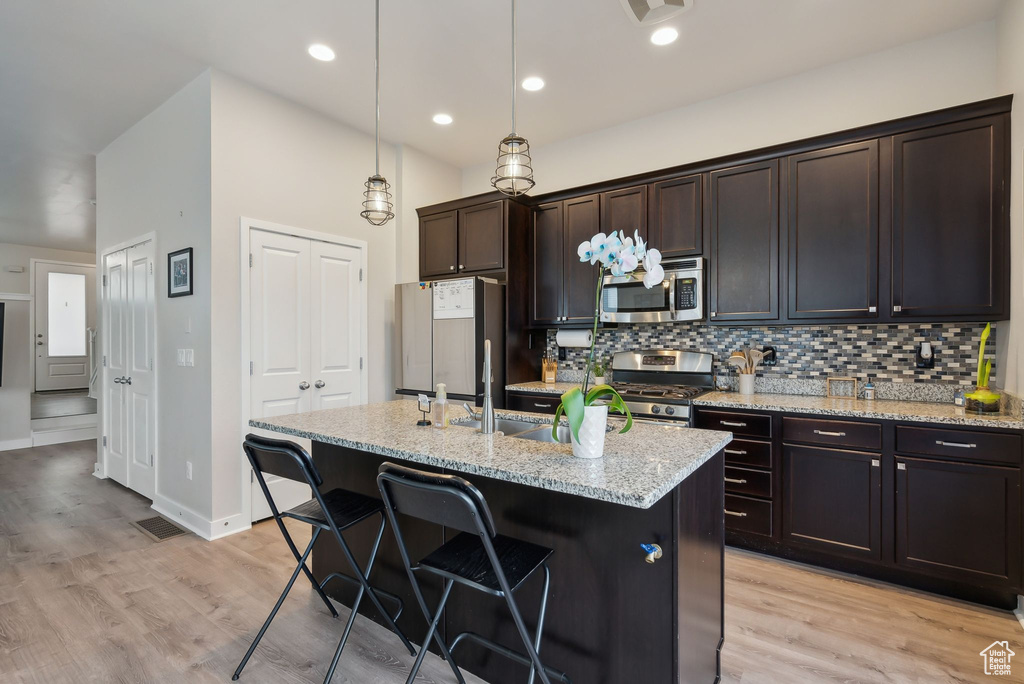 Kitchen featuring a breakfast bar, an island with sink, light wood-style floors, appliances with stainless steel finishes, and tasteful backsplash