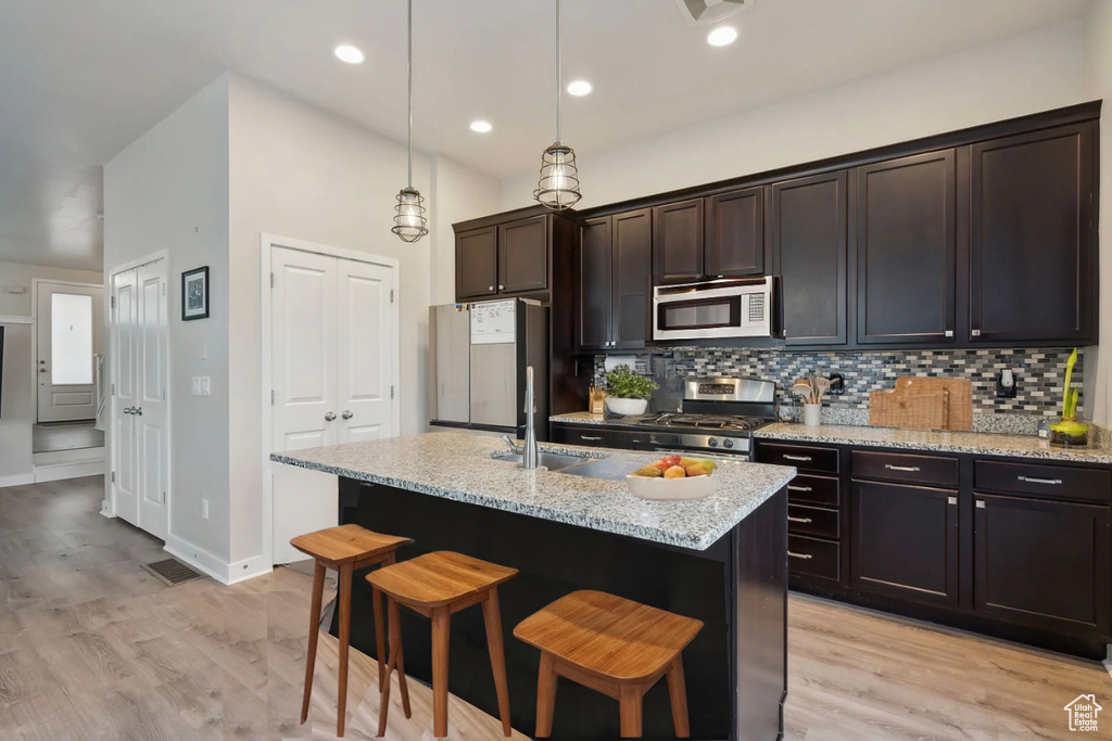 Kitchen with a kitchen bar, light wood-type flooring, a sink, stainless steel appliances, and decorative backsplash