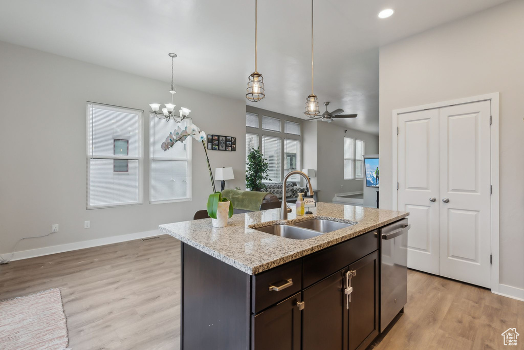 Kitchen with dark brown cabinetry, open floor plan, light wood-type flooring, stainless steel dishwasher, and a sink