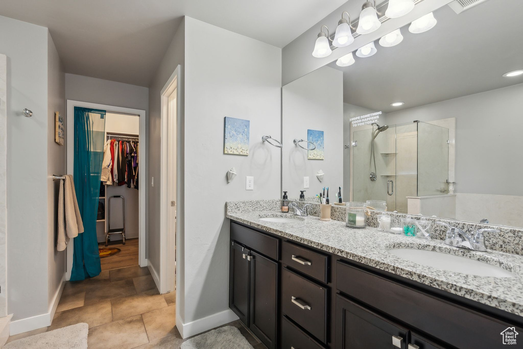 Full bath featuring a walk in closet, a shower stall, double vanity, and a sink