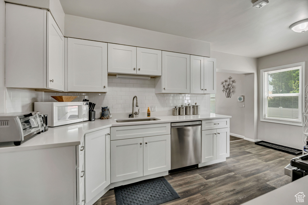 Kitchen featuring stainless steel dishwasher, light countertops, white microwave, decorative backsplash, and white cabinetry