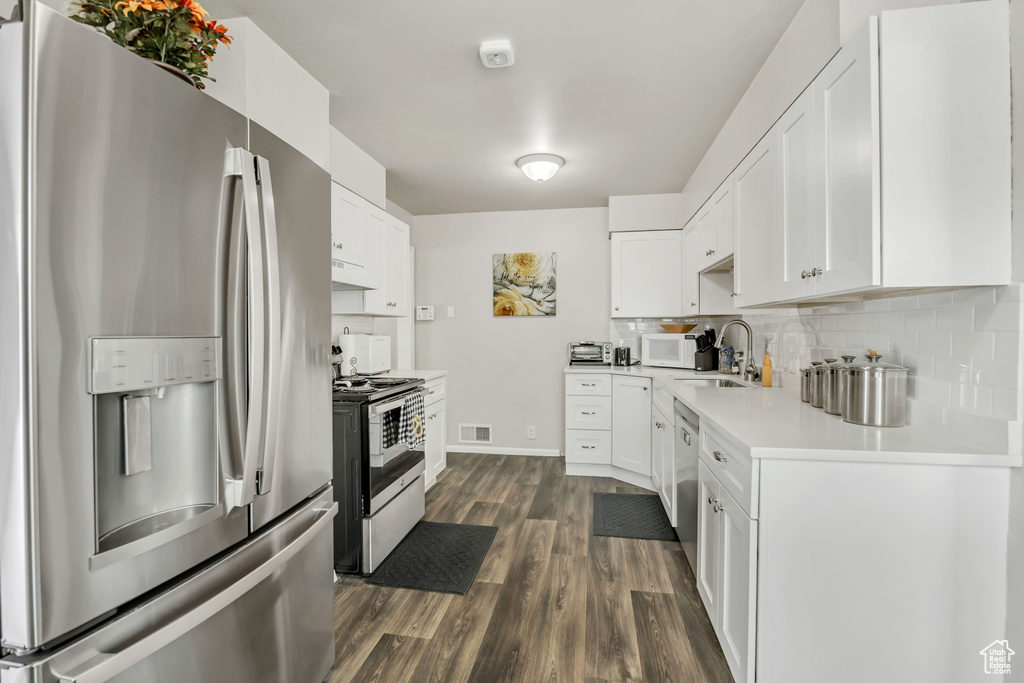 Kitchen with stainless steel appliances, light countertops, dark wood-type flooring, decorative backsplash, and white cabinets