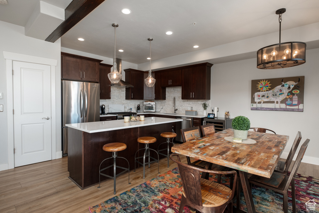 Kitchen featuring appliances with stainless steel finishes, wall chimney exhaust hood, dark brown cabinetry, light wood-style floors, and a center island
