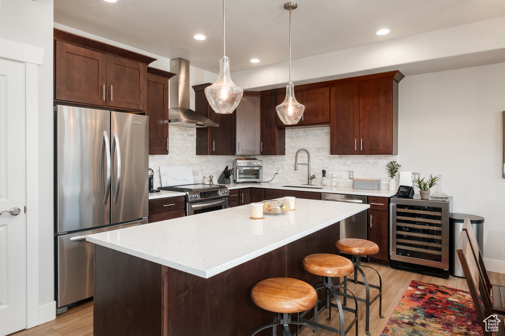 Kitchen featuring appliances with stainless steel finishes, wine cooler, wall chimney exhaust hood, a sink, and light wood-style floors
