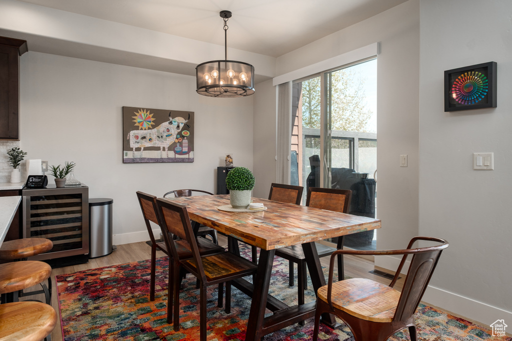 Dining space featuring beverage cooler, baseboards, light wood-style flooring, and a chandelier