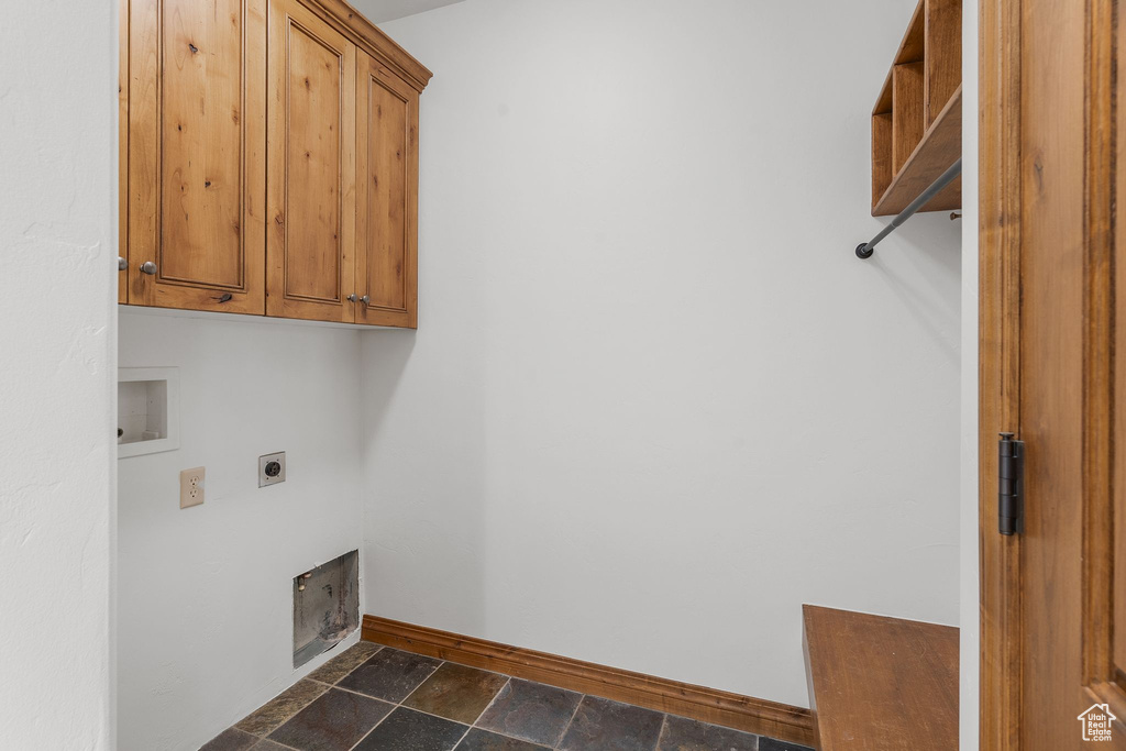 Washroom with electric dryer hookup, cabinet space, stone tile flooring, and hookup for a washing machine